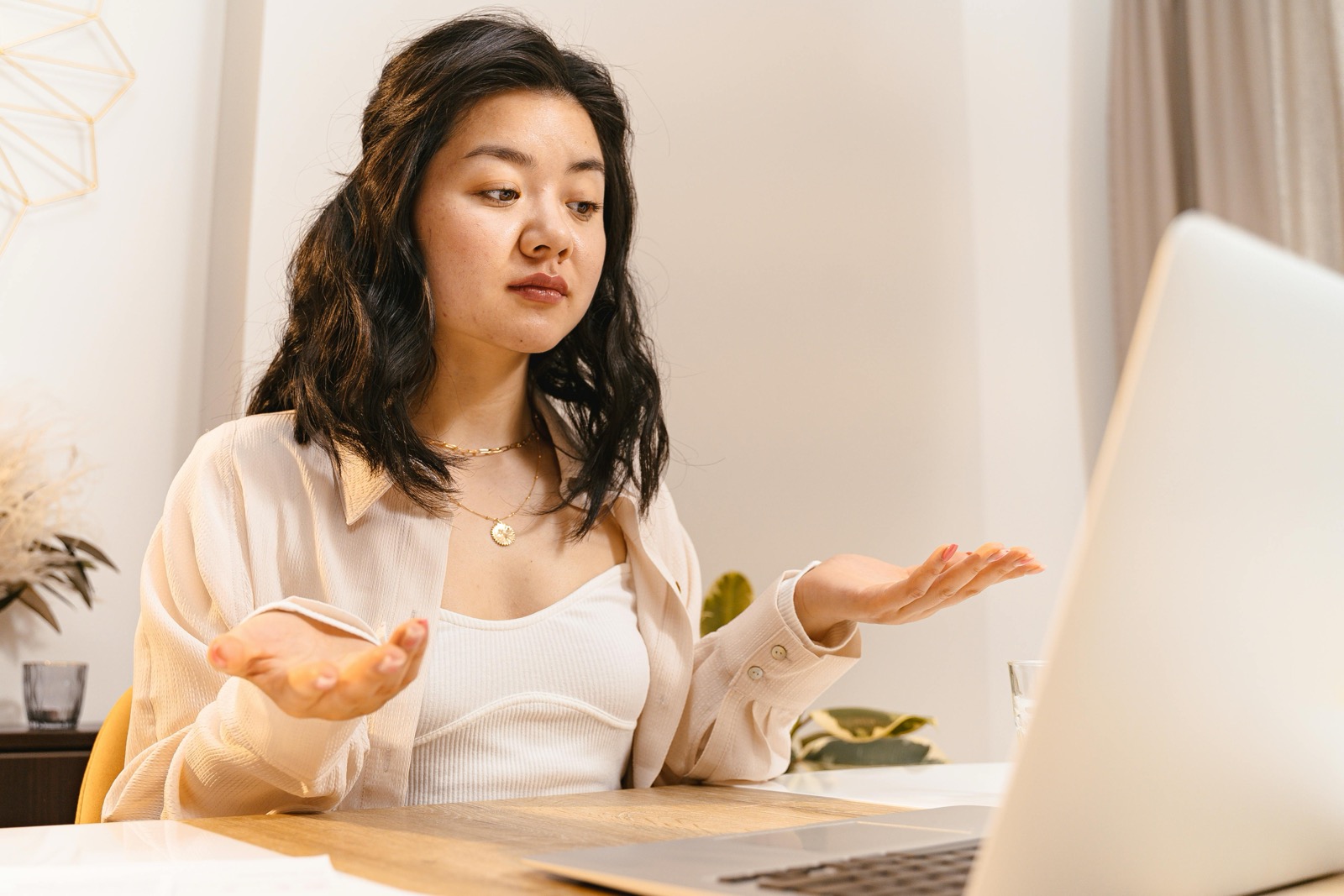 A woman in a white shirt sitting at a laptop with a puzzled expression, paused mid-task.